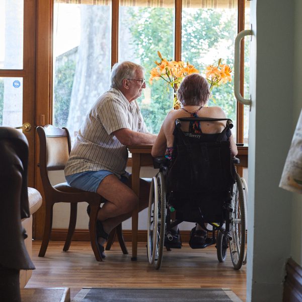 Weavers sitting at a table in their house. One is in a wheelchair