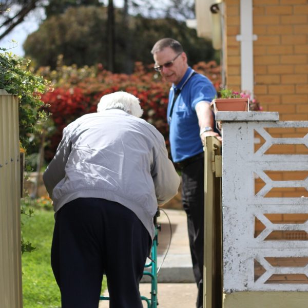Man using a walker passing through a gate held by a carer