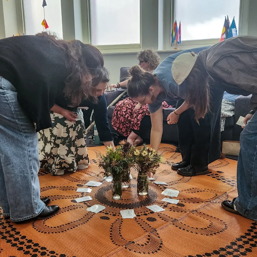 People participating in a workshop placing notes in a circle around some flowers in a vase.